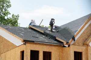 Person safely inspecting a leafy roofline and clearing debris from a gutter beside a home.