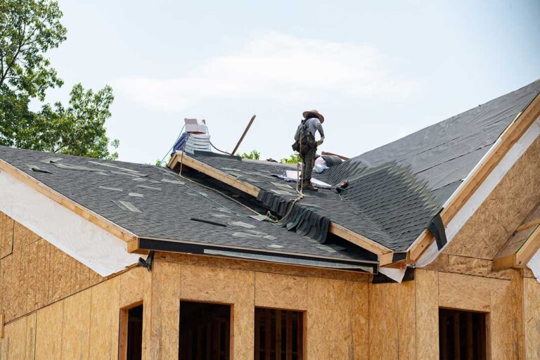 Person safely inspecting a leafy roofline and clearing debris from a gutter beside a home.
